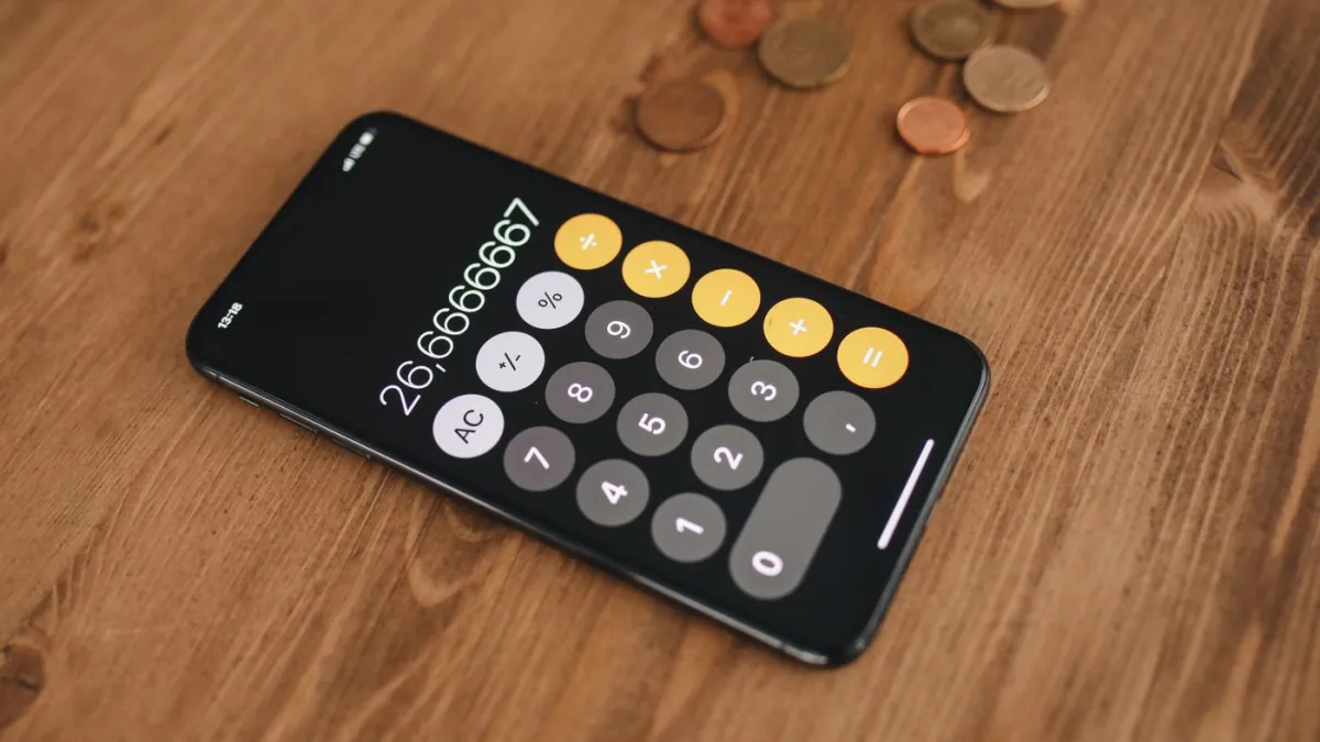 Smartphone calculator beside coins on a wooden table.