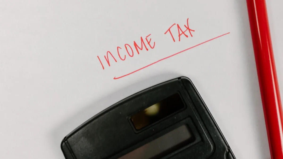 Calculator, red pen and paper labelled Income Tax for payroll calculations.